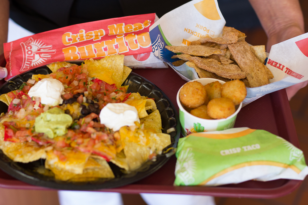 A picture of nachos with sour cream, guacamole, a burrito, and a crisp taco on a red tray