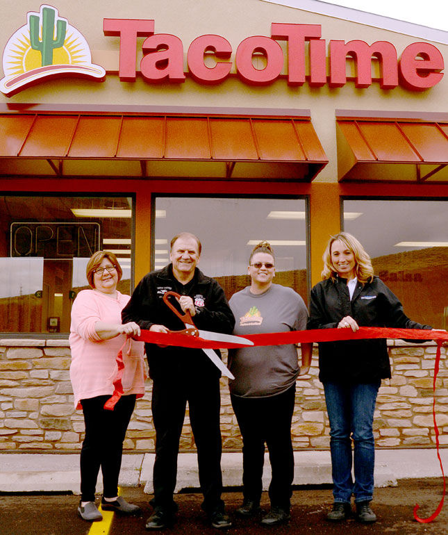 A smiling family cuts a long red ribbon in front of a TacoTime new franchise location